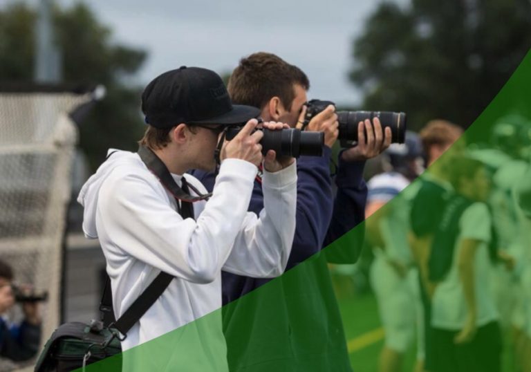 Two students with DSLR cameras taking photos at a football game