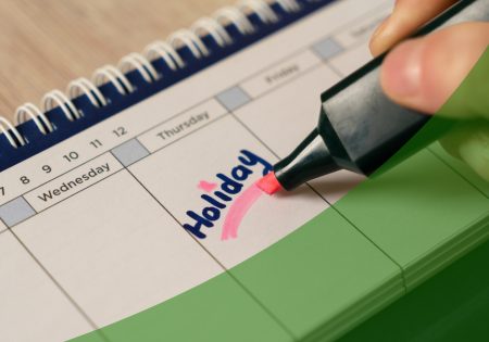 Calendar with someone writing Holiday with a pink highlighter with a green swoosh in the bottom right corner