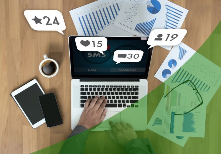 Laptop on a desk with devices, coffee and papers with charts on them. There are digital icons popping up around the screen.