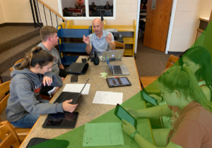Students sitting at a table in the library of a school with devices working on creating content