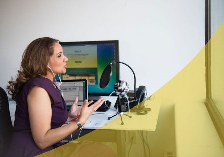 Woman speaking into a microphone at her desk with laptop and podcasting setup