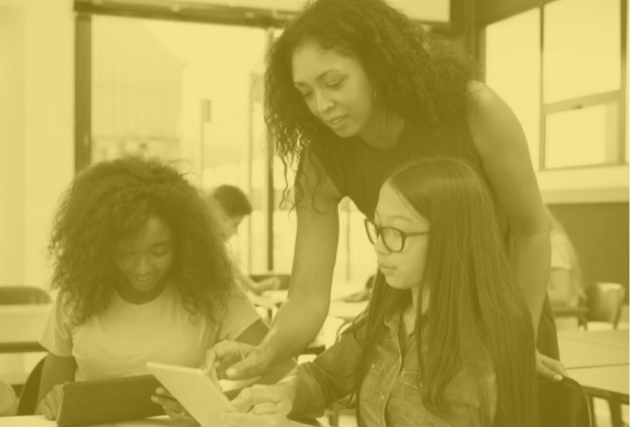 A teacher helping two girl students with an assignment.
