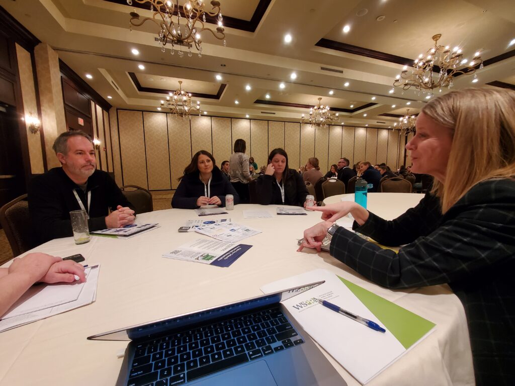 Class Intercom President, Jill, sitting at a table with other education professionals at a conference.