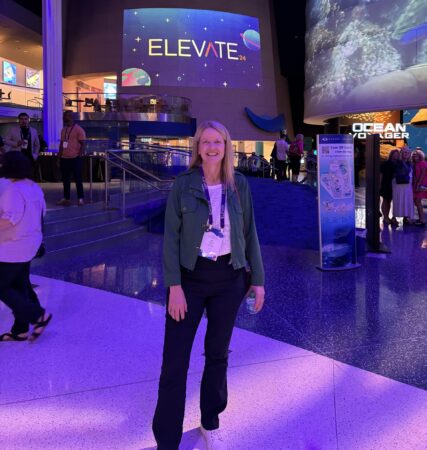 Dr. Jill Johnson stand in the center of the Georgia aquarium in front of a large projection that reads, "Elevate".