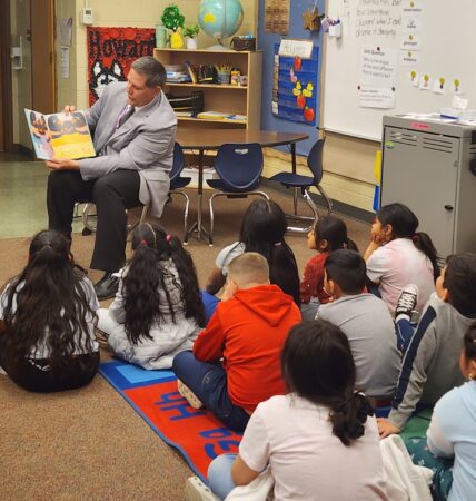 A school superintendent reads to a classroom of elementary school students.