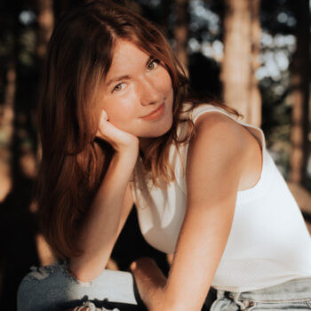 Abigail Young, a senior at Nebraska Christian Schools and author of the blog, smiles gently while posing outdoors in a white top and ripped jeans, with trees in the background.