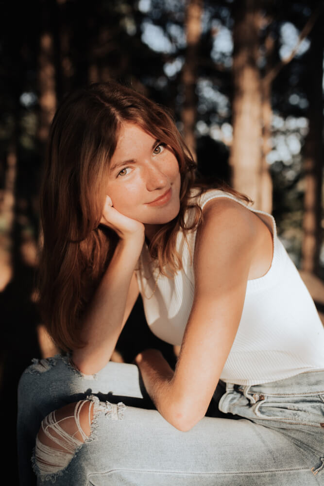 Abigail Young, a senior at Nebraska Christian Schools and author of the blog, smiles gently while posing outdoors in a white top and ripped jeans, with trees in the background.