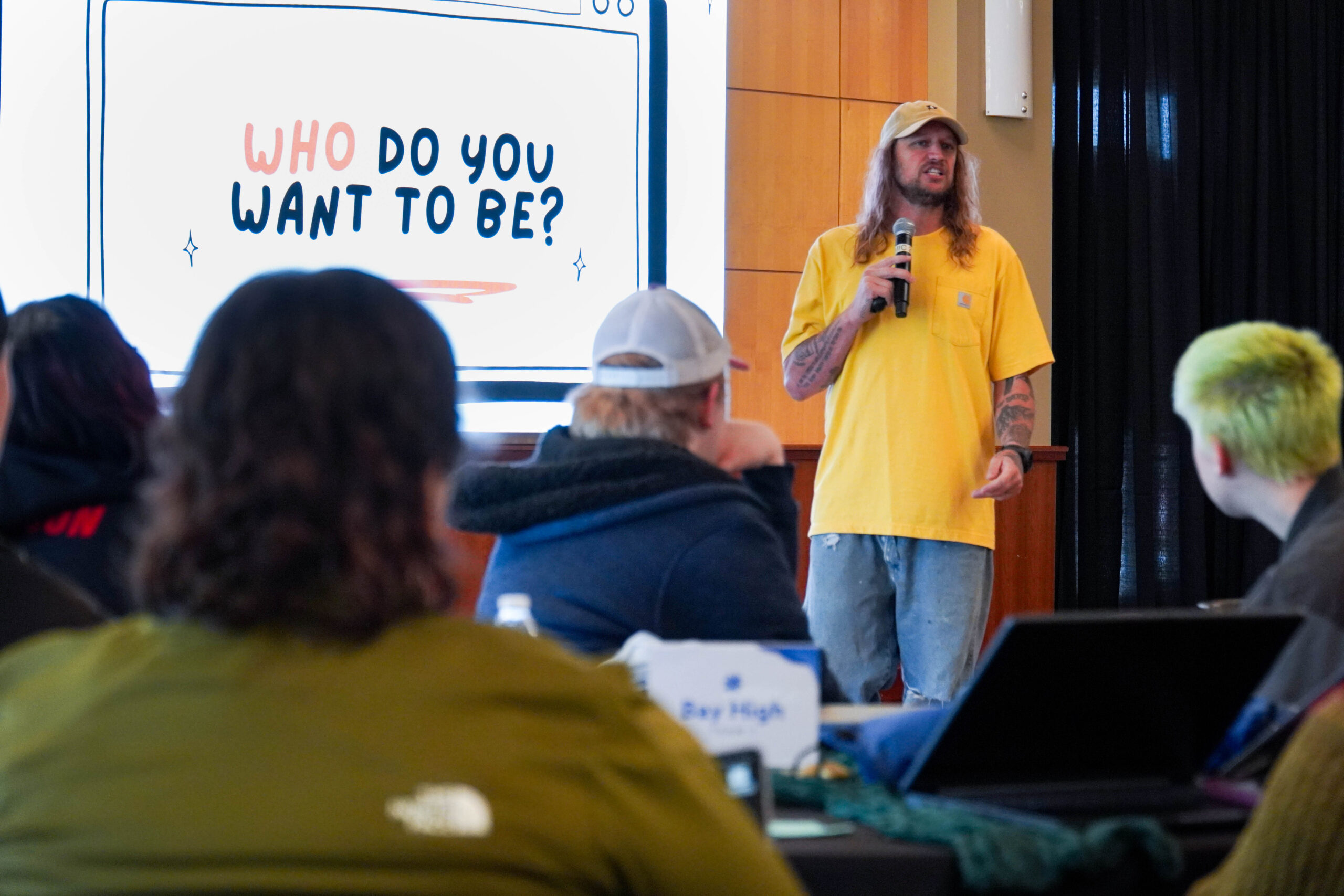Mike Smith presents to a group of students at the 2025 Content Generation Workshop. A screen in the back reads, "Who do you want to be?" 
