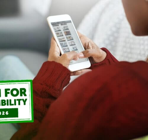 A girl in a red sweater sits on a couch scrolling on her phone. There a graphic overlay that reads, "All in for Accessibility in 2026" almost like a stamp.