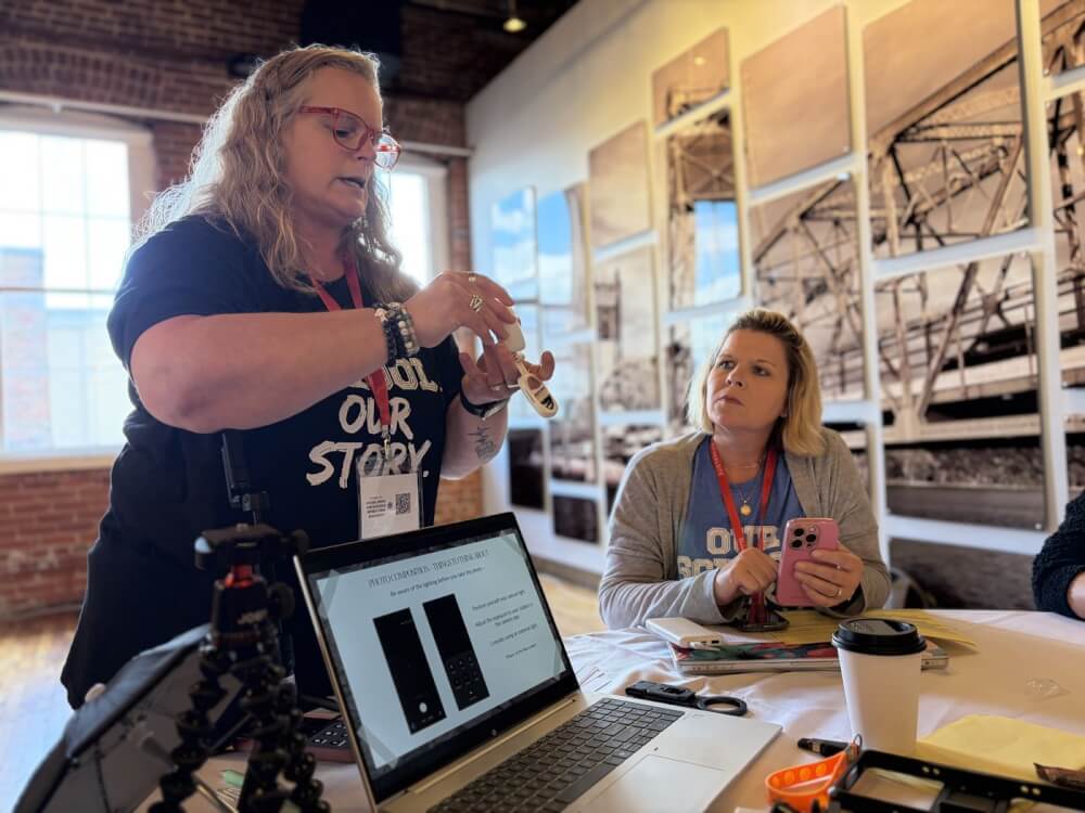 A presenter demonstrates mobile photo composition techniques on a laptop while a retreat attendee looks on.